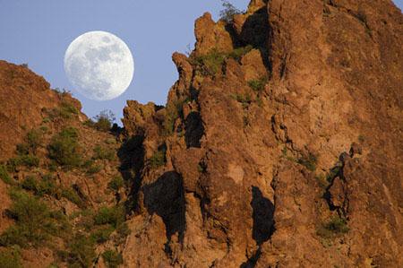 A gibbous moon rises as seen through the cliffs of the Superstition Mountains